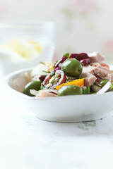 Salad with tuna, green olives and cherry tomatoes. Bright wooden background. Close up. Copy space.