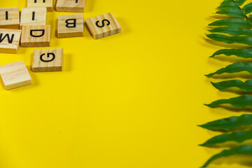 Beautiful bright summer yellow background with  green tropical plant branch and wooden alphabet...