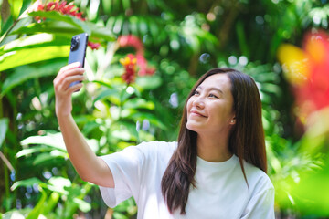 Portrait image of a young woman using mobile phone to take a selfie in the garden