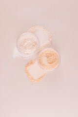 Two glass cosmetic open jars with loose powder of natural and light tones stand on the swatches. top vertical view. texture of decorative cosmetics.