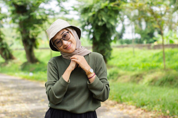 A joyful young girl wearing a green hat and sweater smiles brightly while standing in a lush green...