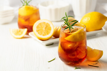 Iced tea or alcoholic cocktail with ice, rosemary and lemon slices on the white table.