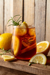 Iced tea or alcoholic cocktail with ice, rosemary and lemon slices on a old wooden table.