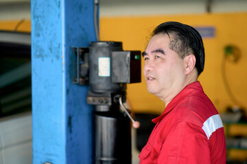 Senior asian technician working with car lifting machine in car garage.