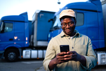 Professional truck driver holding smart phone in front of the trucks.
