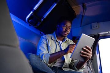 Truck driver sitting in the cabin and communicating with his family via digital tablet.