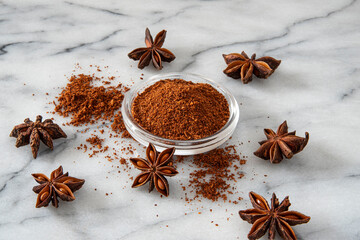 Close-up of dried star anise seeds and powder on a white marble background