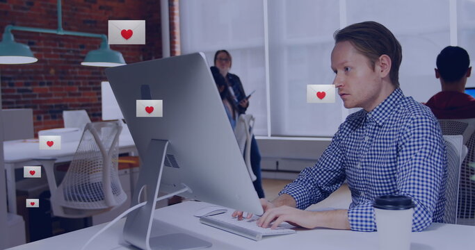 Image of heart shape in envelopes over biracial man working on desktop in office