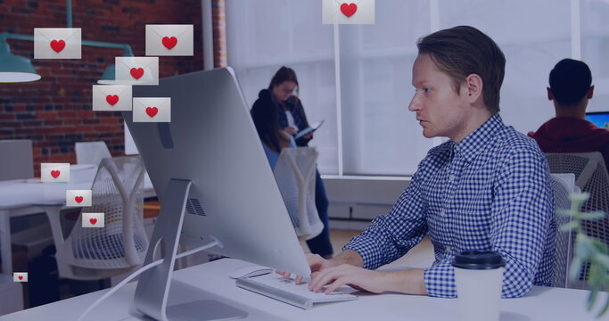 Image of heart shape in envelopes over biracial man working on desktop in office