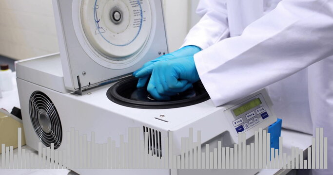 A person in lab coat and blue gloves is operating a centrifuge machine