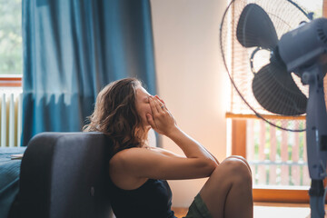 Young woman suffering from heat sitting at home on the floor in front of a fan