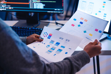 software developer reviews UX/UI design diagrams while coding at a workstation
