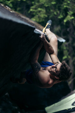 Shirtless climber with tattoo climbing a steep boulder