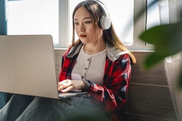Porter Beautiful serious Asian teenager girl in headphones using laptop for online education