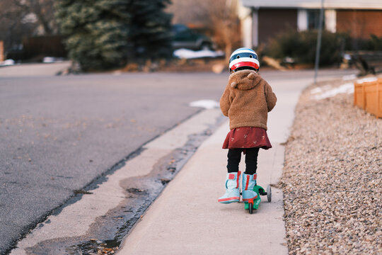 Child riding scooter on a neighborhood sidewalk in winter