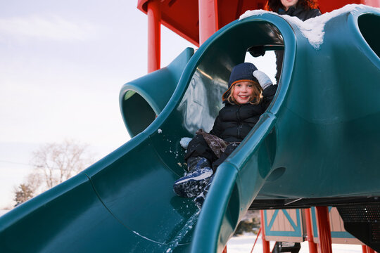 Smiling child sliding down a playground slide in winter