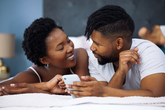 Morning, mobile and black couple lying on bed for social media, connection or relax in bedroom. Online, romantic man and happy woman with love for text, browsing internet or weekend rest in home