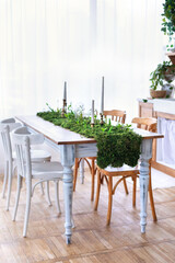 Interior home kitchen in scandi style. Dining room with wooden furniture. Dining table and chairs in modern home with elegant decor. Festive decorated table with of green moss, plants and candles. 