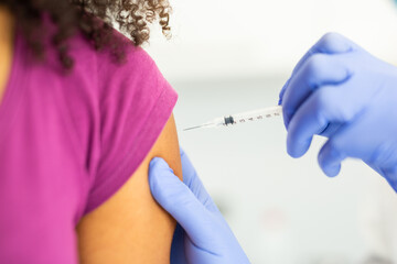 Close-up of a doctor administering a vaccine injection into a patient's arm. The patient is wearing...