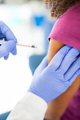 Close-up of a doctor administering a vaccine injection into a patient's arm. The patient is wearing...