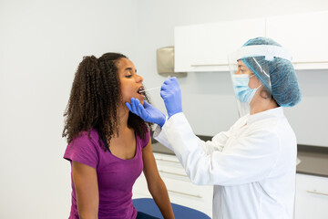 Healthcare worker administering a COVID-19 test by taking a swab sample from a patient's mouth. Patient seated while a healthcare worker is wearing protective gear.