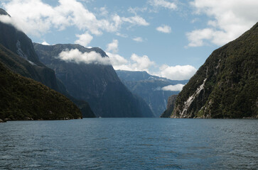 A breathtaking scene of tranquil sea nestled amidst towering mountains, under a vast sky and clouds over mountains, Milford Sound, New Zealand