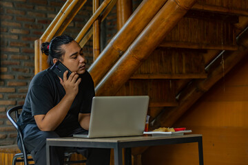 Young Asian man, digital nomad working remotely from cafe, using laptop and smartphone. young Asian...
