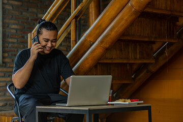 Young Asian man, digital nomad working remotely from cafe, using laptop and smartphone. young Asian...