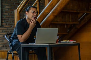 Young Asian man, digital nomad working remotely from cafe, using laptop and smartphone. young Asian...