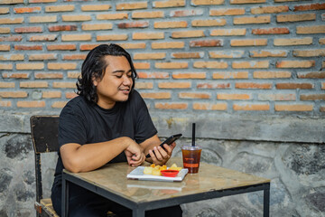 Young Asian man, digital nomad working remotely from cafe, using laptop and smartphone. young Asian...