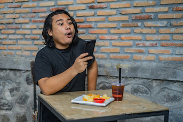 Young Asian man, digital nomad working remotely from cafe, using laptop and smartphone. young Asian...