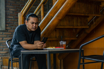 Young Asian man, digital nomad working remotely from cafe, using laptop and smartphone. young Asian...