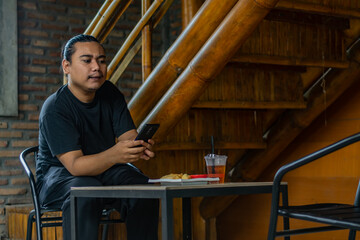 Young Asian man, digital nomad working remotely from cafe, using laptop and smartphone. young Asian men are hanging out in a cafe with an industrial theme