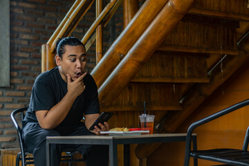 Young asian men, digital nomad working remotely from a cafe, using  smartphone.