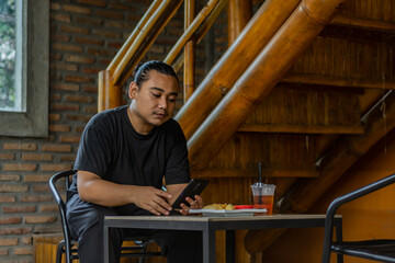 Young asian men, digital nomad working remotely from a cafe, using  smartphone.