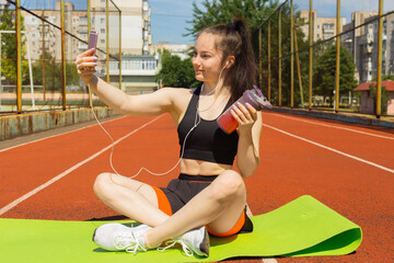 Sport and technology. A beautiful young woman with a ponytail sitting resting after workout during...