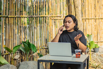 Young asian men, digital nomad working remotely from a cafe, drinking coffee and using laptop.