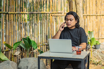 Young asian men, digital nomad working remotely from a cafe, drinking coffee and using laptop.
