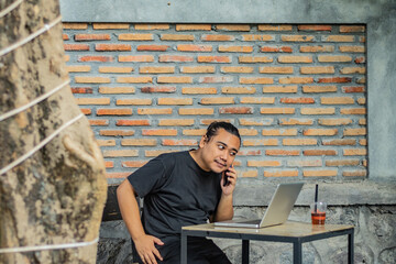 Young asian men, digital nomad working remotely from a cafe, drinking coffee and using laptop.