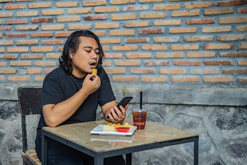 Young Asian man, digital nomad working remotely from cafe, using laptop and smartphone. young Asian...