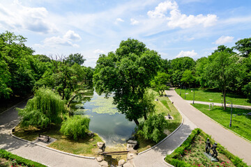 Vivid landscape in Nicolae Romaescu park from Craiova in Dolj county, Romania, with lake, waterlillies and large green tres in a beautiful sunny spring day with blue sky and white clouds