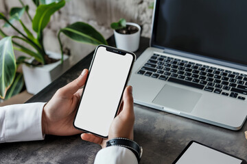 mockup smartphone iphone with empty blank screen in men hand on desktop, laptop background