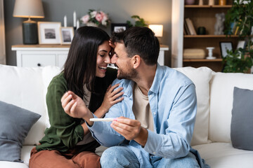 Expectations, wanted pregnancy. Young happy couple man and woman sitting at home on sofa holding...