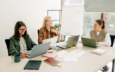 Young women using laptops working in the office, brainstorming and discussing business strategy.