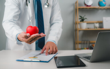 Doctor showing a red heart at hospital office, Healthcare worker and doctor service, Digital laptop in modern office, Medical technology concept, Health insurance concept, Health planning concept.