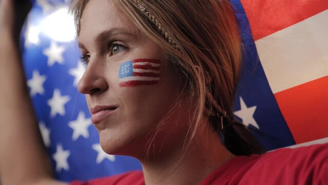 USA sports fan. Close-up of woman with US flag in her hands and on her face watching match, competition, game and cheering for US team