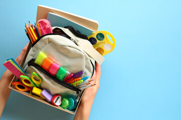 Donation box with backpack with school supplies on a blue background. Charity concept.