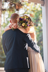 Two individuals embracing each other while holding a bunch of flowers.
