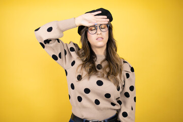 Young beautiful brunette woman wearing french beret and glasses over yellow background Touching forehead for illness and fever, flu and cold, virus sick