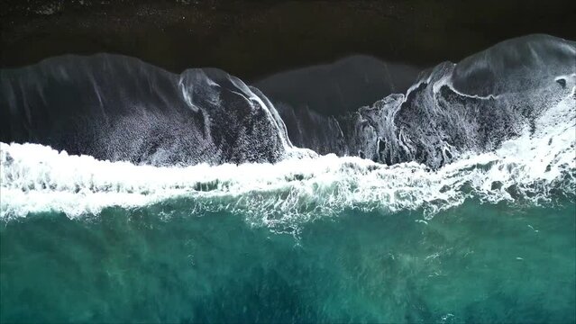 Horizontal Drone Shot of Black Sand Beach in Indonesia. Aerial View Top Down waves crushing flying slowly up with plastic at the beach.